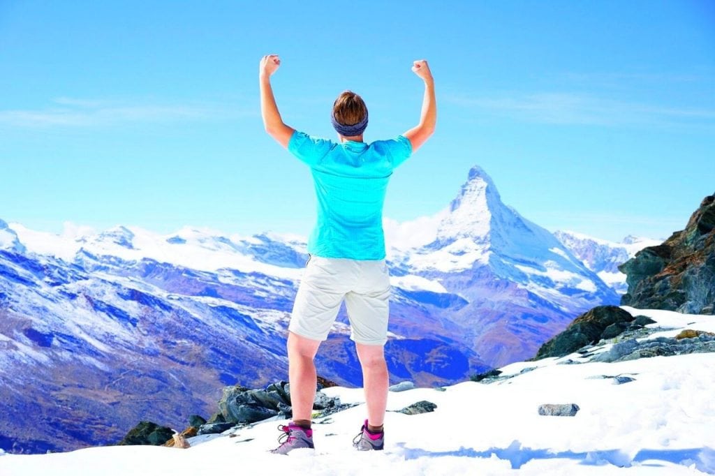 Hombre de espaldas en la cima de una montaña con los brazos triunfales en alto