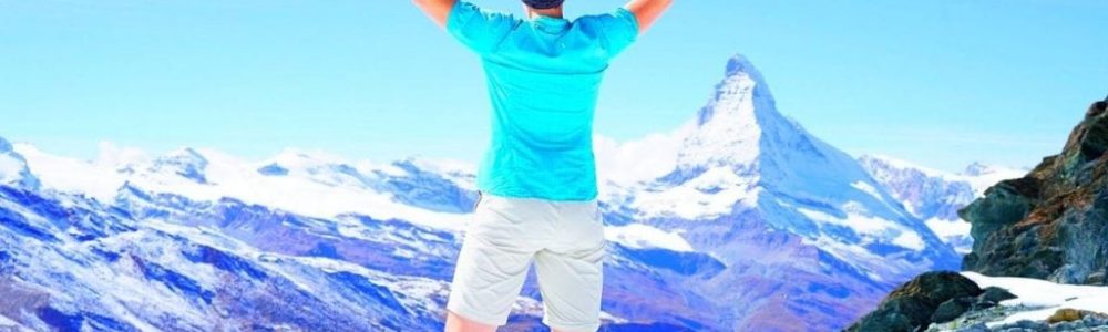Hombre de espaldas en la cima de una montaña con los brazos triunfales en alto