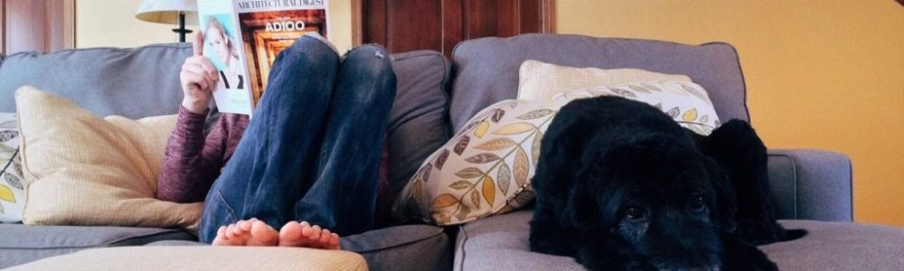 Mujer tumbada en un sofá leyendo una revista y perro negro tumbado a su lado
